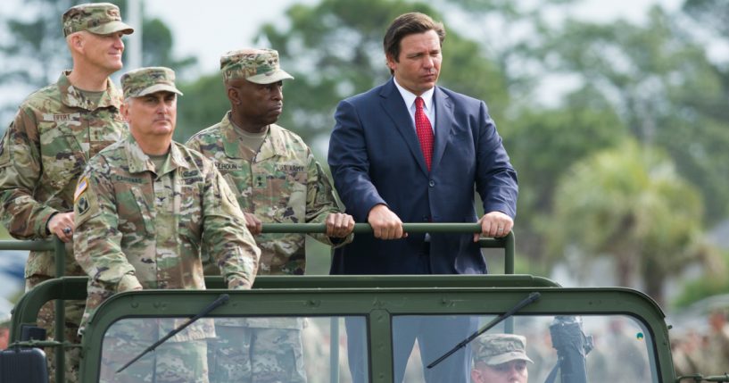 Three soldiers standing on military vehicle with Ron DeSantis